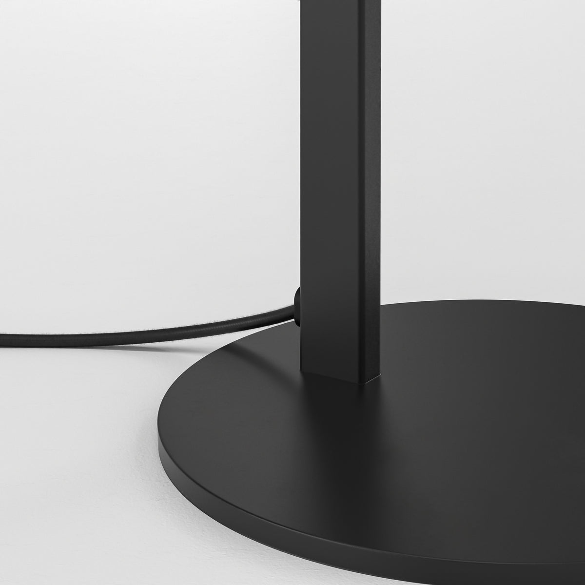 Black lamp base and pole with a black power cord against a white background