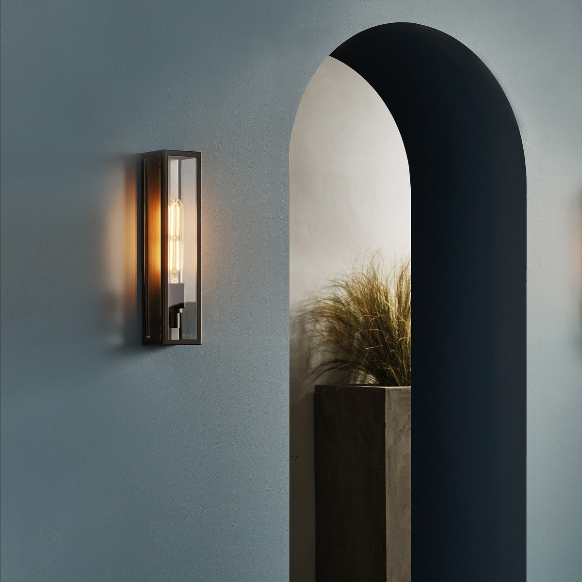 A wall sconce with a rectangular glass shade and an exposed filament bulb, mounted on a blue wall