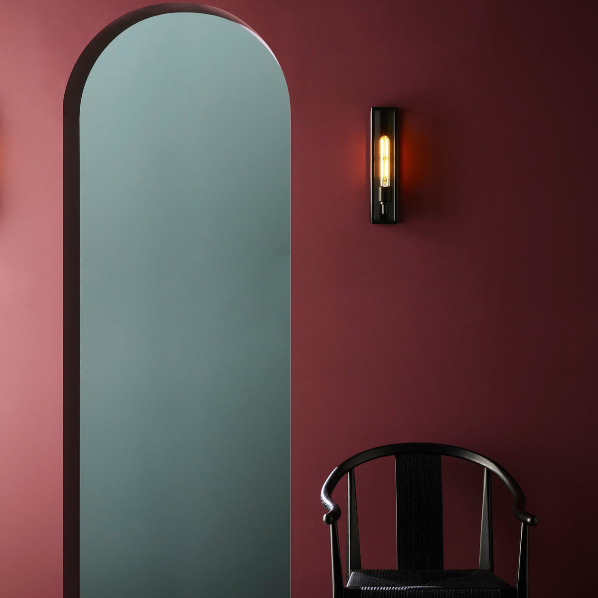 Archway with light blue interior, dark red wall with a black wall light, and a black wooden chair