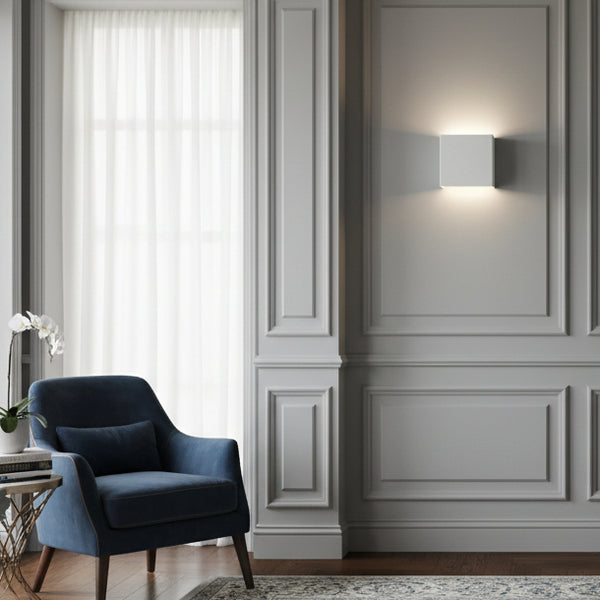 Square white wall light on a grey paneled wall above a blue armchair