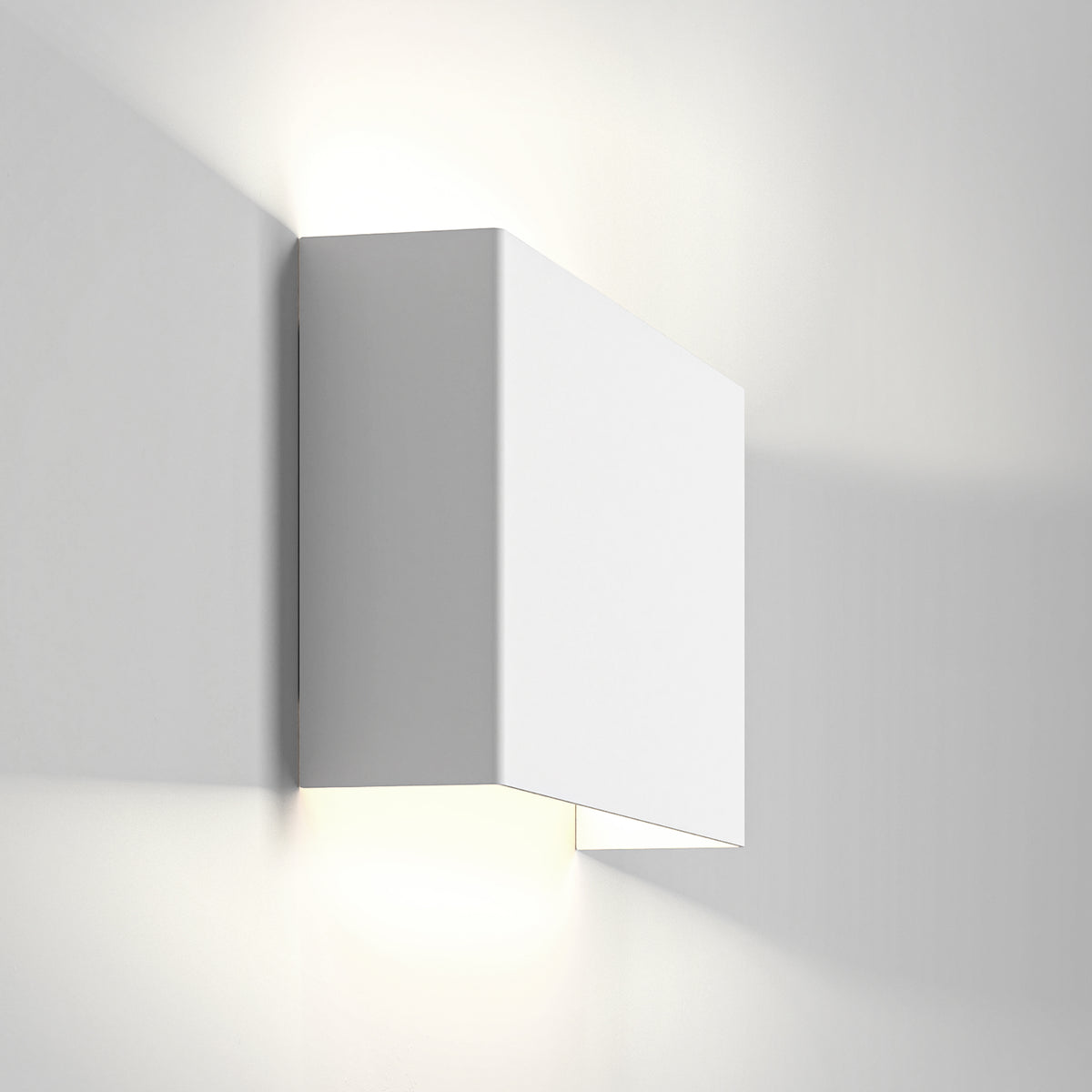 White rectangular wall light fixture casting light upwards and downwards on a white wall