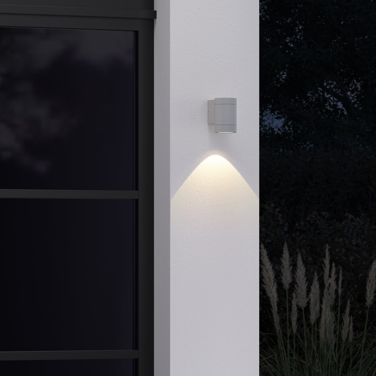 Outdoor wall light illuminating a white wall next to a dark window frame and tall grasses at night