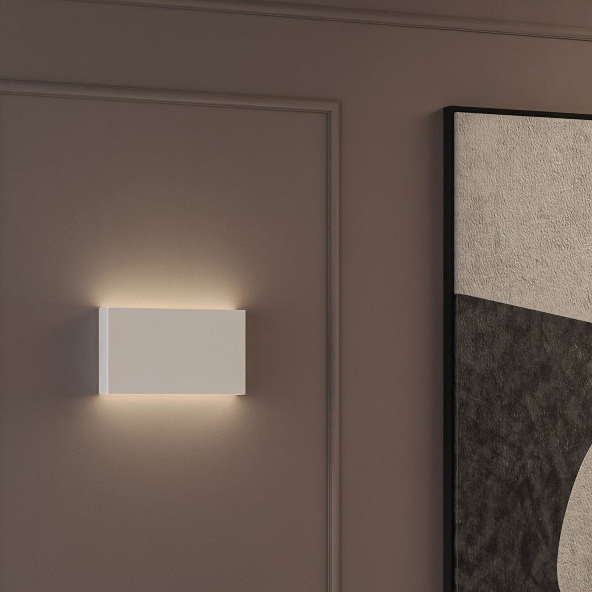 Rectangular white wall light with warm glow on a brown wall next to a framed abstract painting