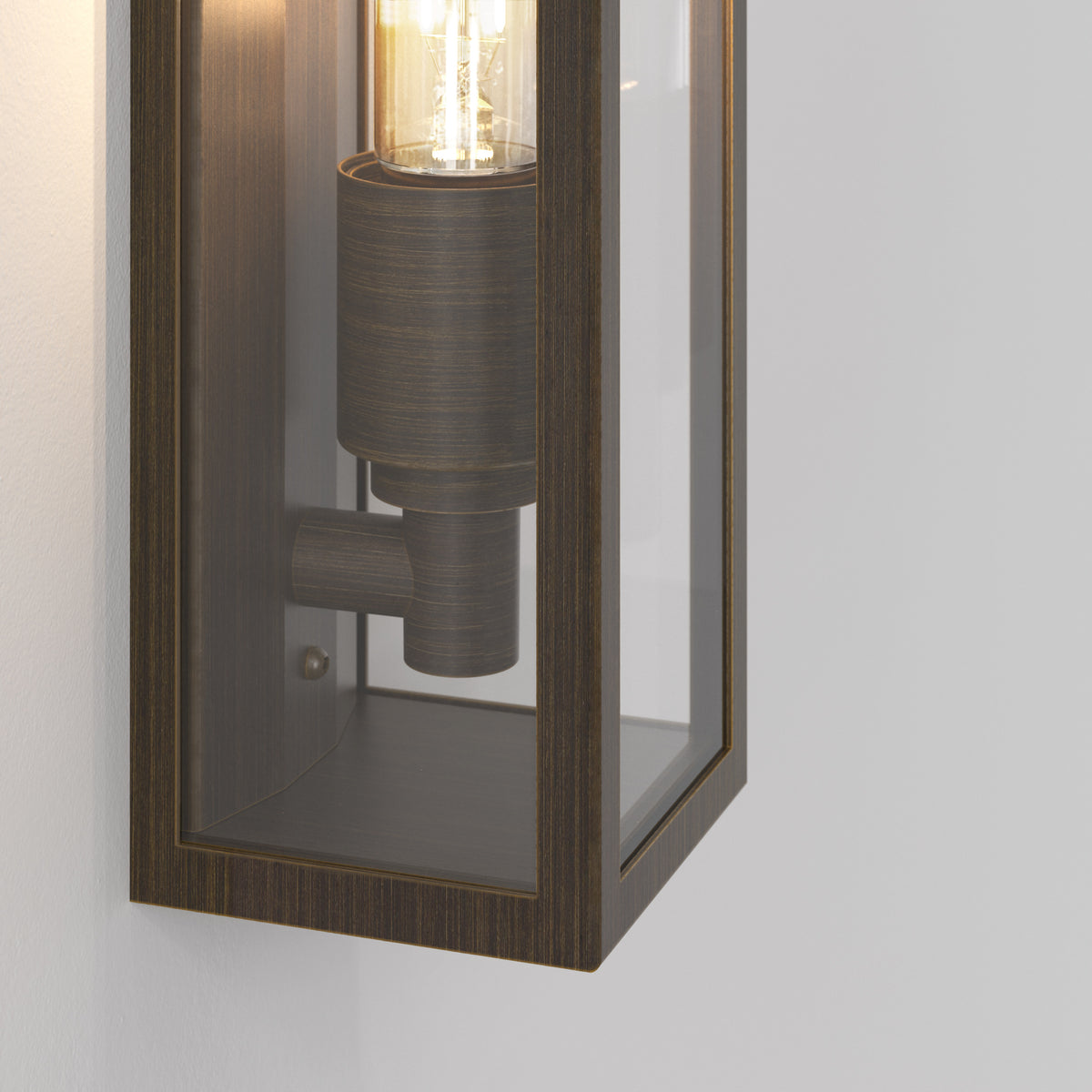 Close up of a bronze outdoor wall light with clear glass panels and an exposed filament bulb