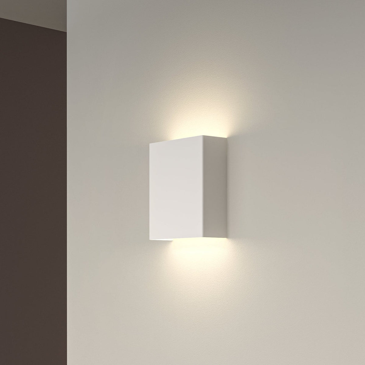 White rectangular wall light fixture casting light upwards and downwards on a light grey wall