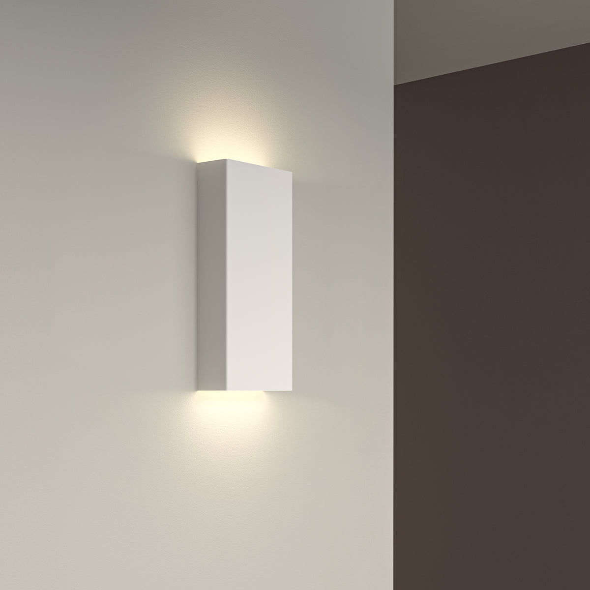 White rectangular wall light fixture casting warm light upwards and downwards on a light grey wall