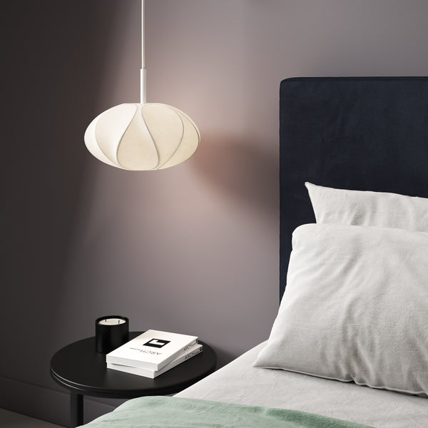 White pendant light above a black side table with a candle and books next to a bed with white pillows
