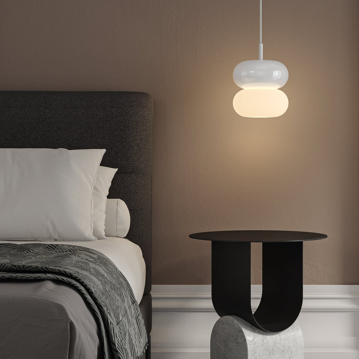Bedroom with a bed, pillows, and a blanket. A black side table with a concrete base and a white pendant light.