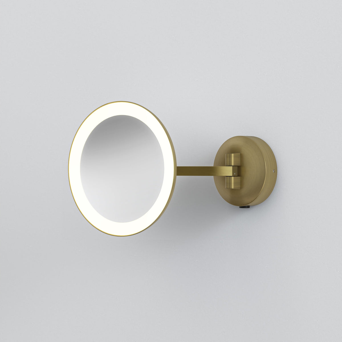 Round illuminated magnifying mirror with a brass finish, mounted on a white wall