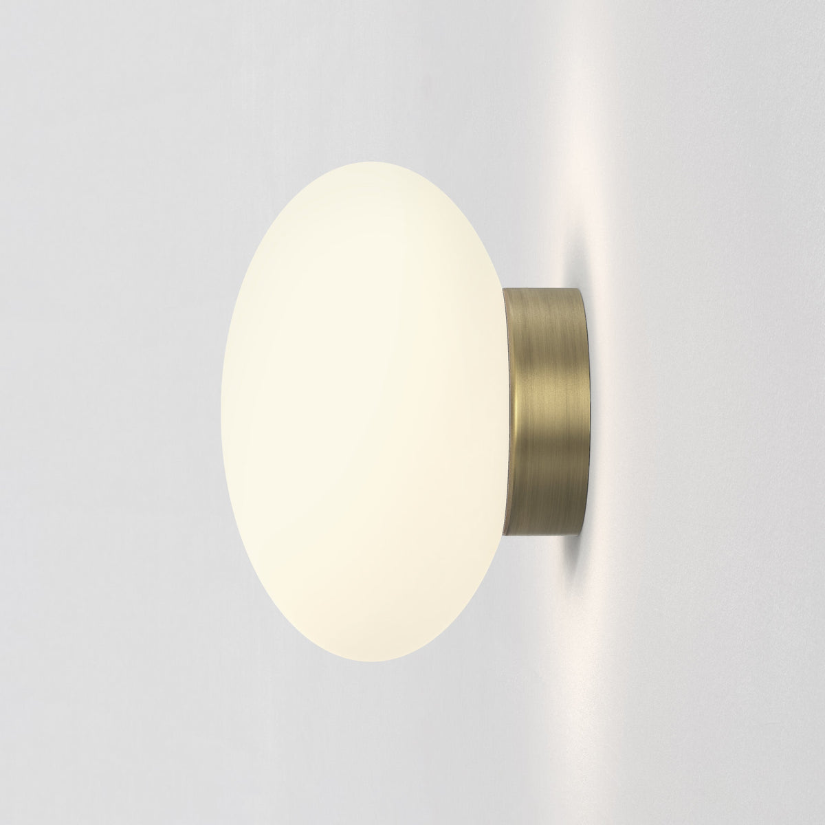 Round wall light with a white glass globe and a brass base, emitting a warm glow on a white wall