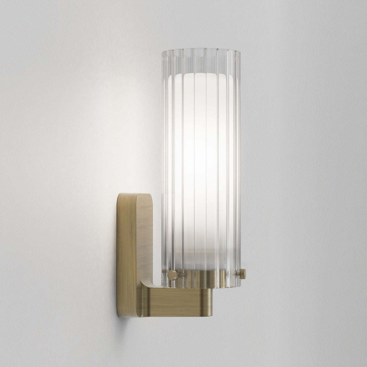 Wall-mounted light fixture with a brass base and a fluted glass shade