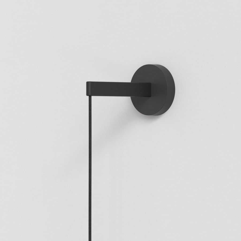 Black wall-mounted light fixture with a round base and a rectangular arm holding a black cord