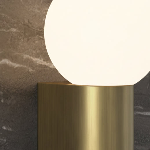 Close up of a brass wall sconce with a round white globe light against a dark marble wall