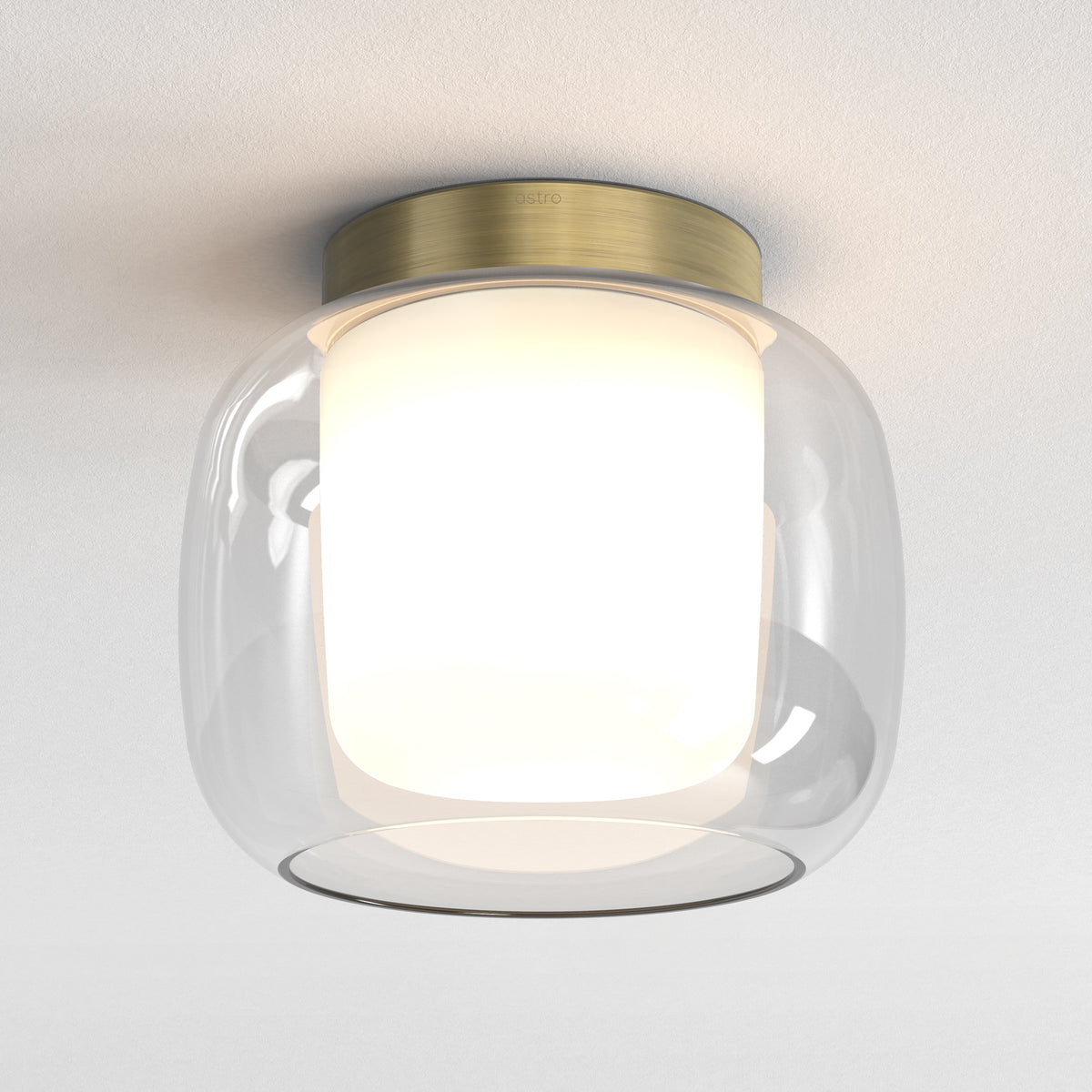 Astro ceiling light with a clear glass shade and a brass base, illuminating a white ceiling