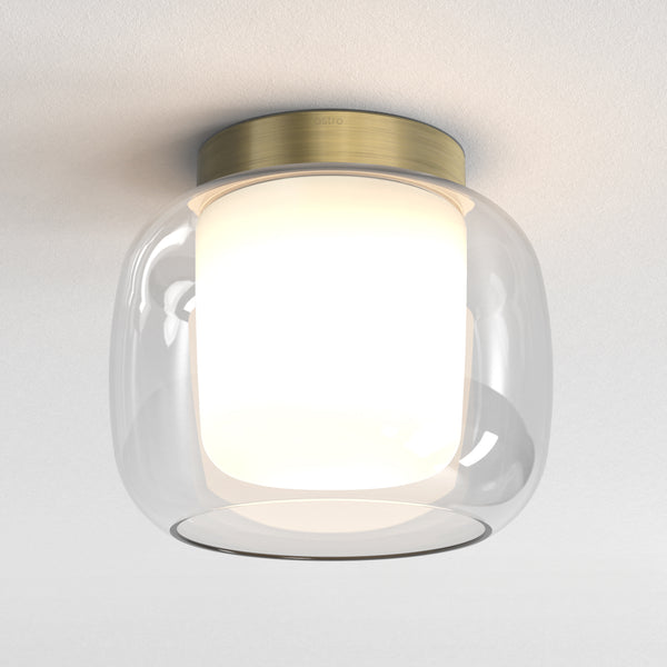 Astro ceiling light with a clear glass shade and a brass base, illuminating a white ceiling