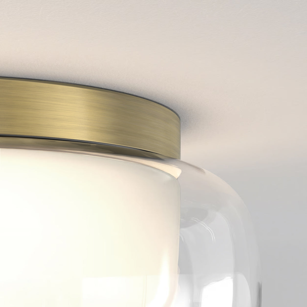 Close-up of a ceiling light fixture with a brushed brass base and a clear glass shade