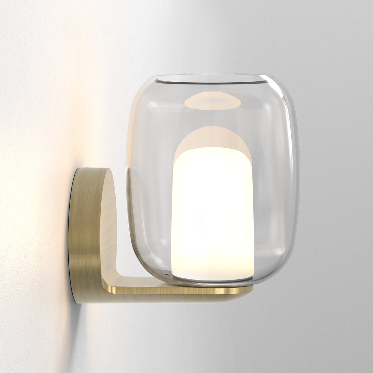 Modern wall light with a clear glass shade and a brushed brass base, illuminating a white wall