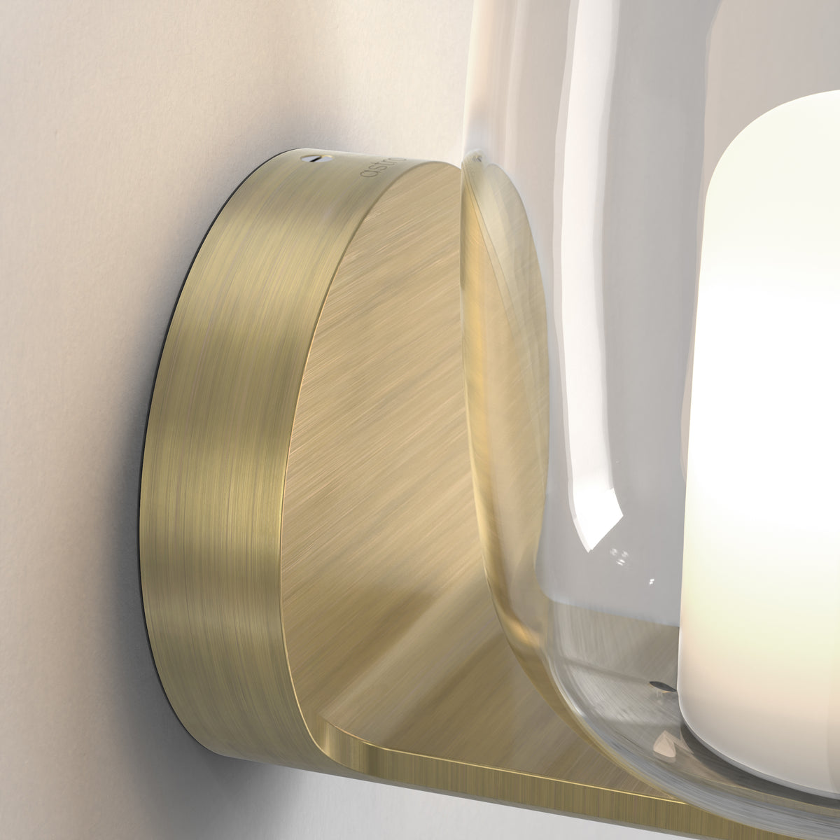 Close-up of a brushed brass wall light with a clear glass shade and an illuminated white bulb