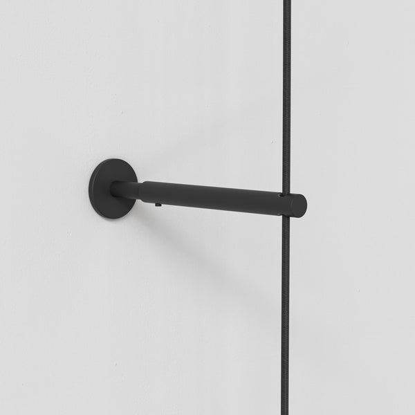 Black wall-mounted light fixture with a cylindrical arm and a fabric-covered cable