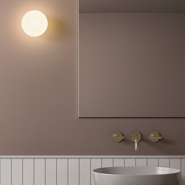 Bathroom with a round wall light, a mirror, a brass faucet, and a gray sink