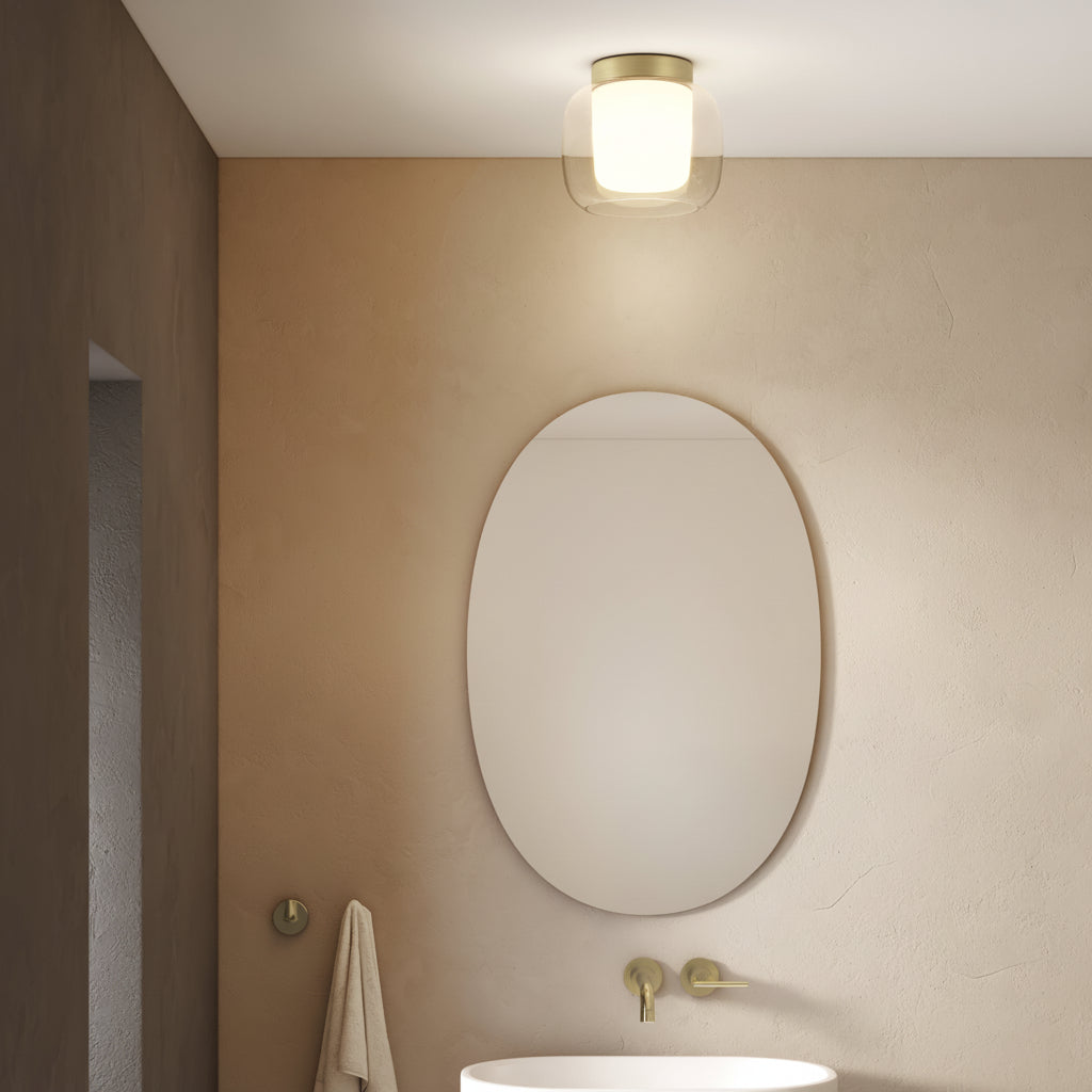 Bathroom with oval mirror, white sink, brass faucet, and ceiling light
