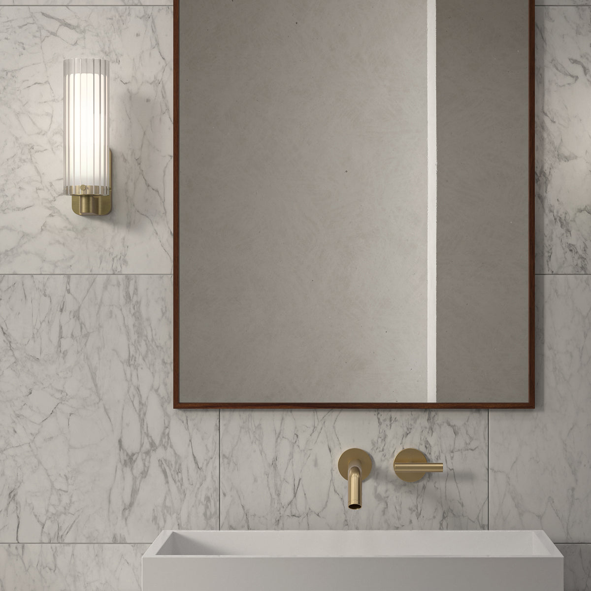 A bathroom with a white marble wall, a rectangular mirror, a white sink, and a gold faucet