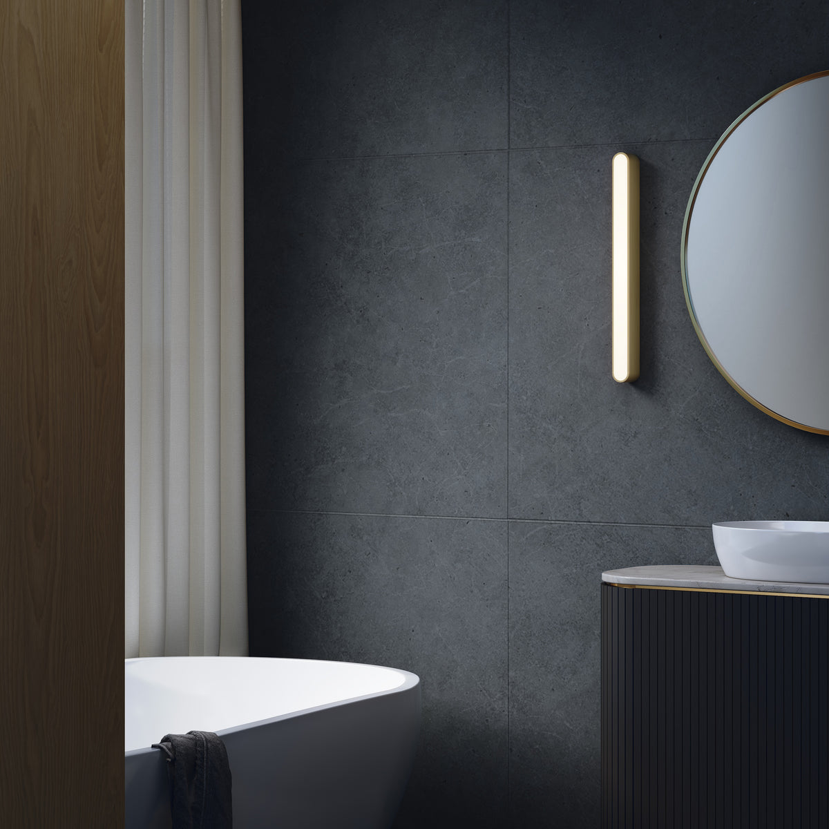 Bathroom with dark grey tiled wall, white bathtub, black vanity with white sink, and round mirror