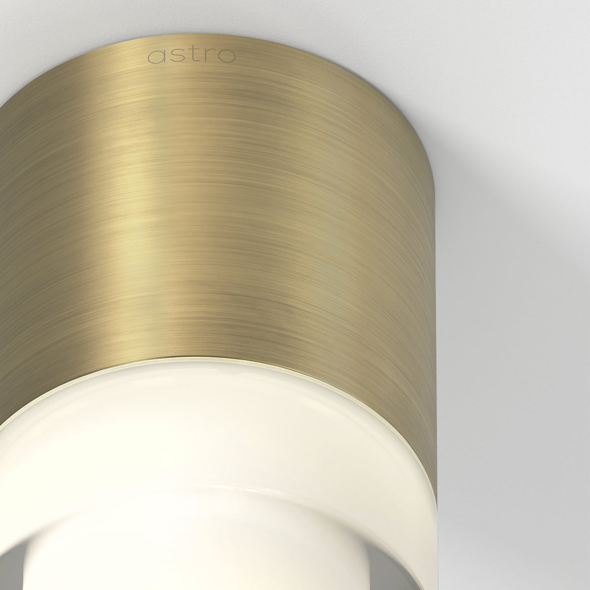 Astro branded cylindrical brass light fixture with a glowing white diffuser