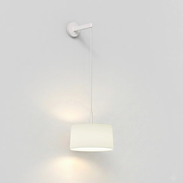 White wall sconce with a cylindrical fabric shade hanging from a thin rod, casting a warm glow downwards