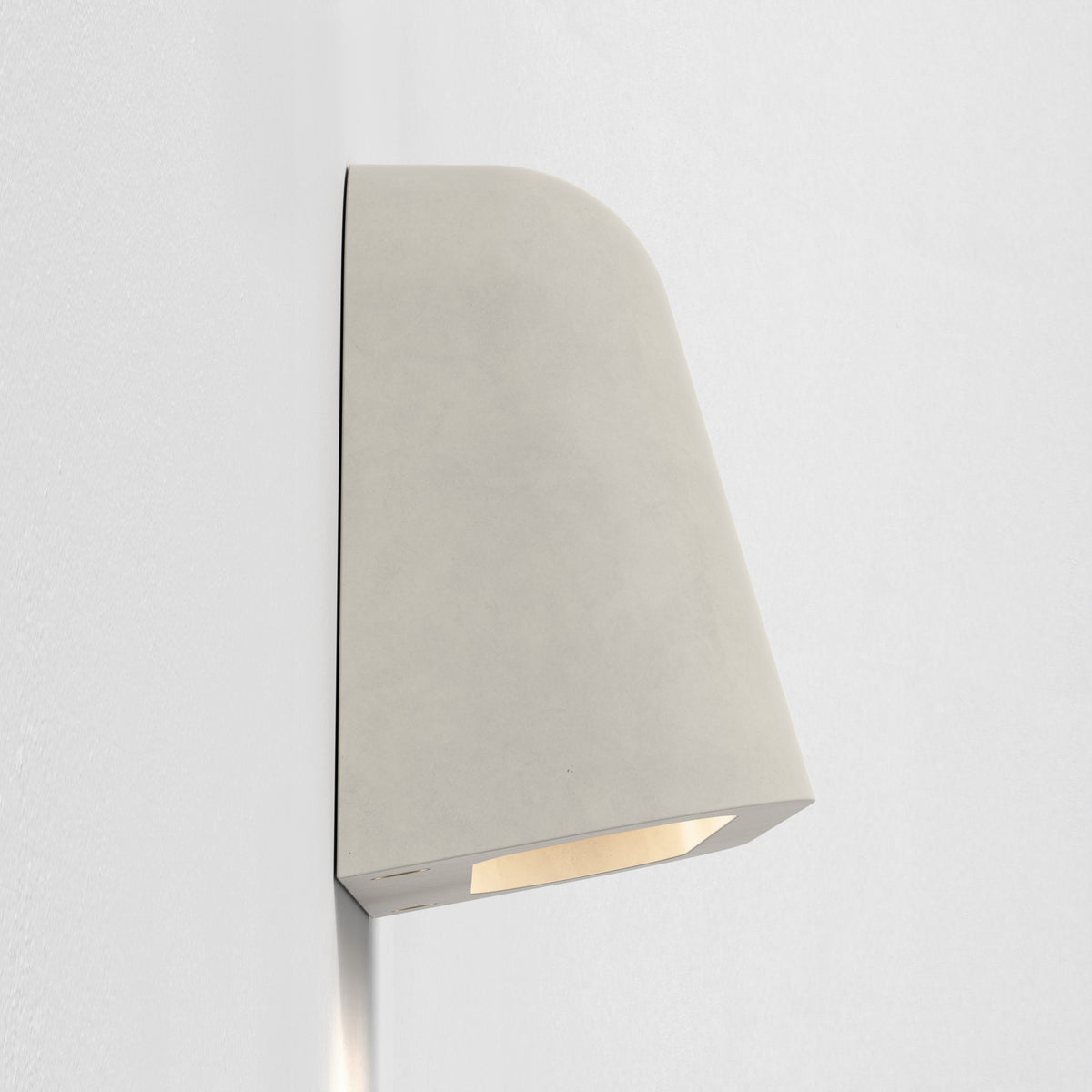 Light grey wall light with a curved top edge and a rectangular opening at the bottom emitting warm light