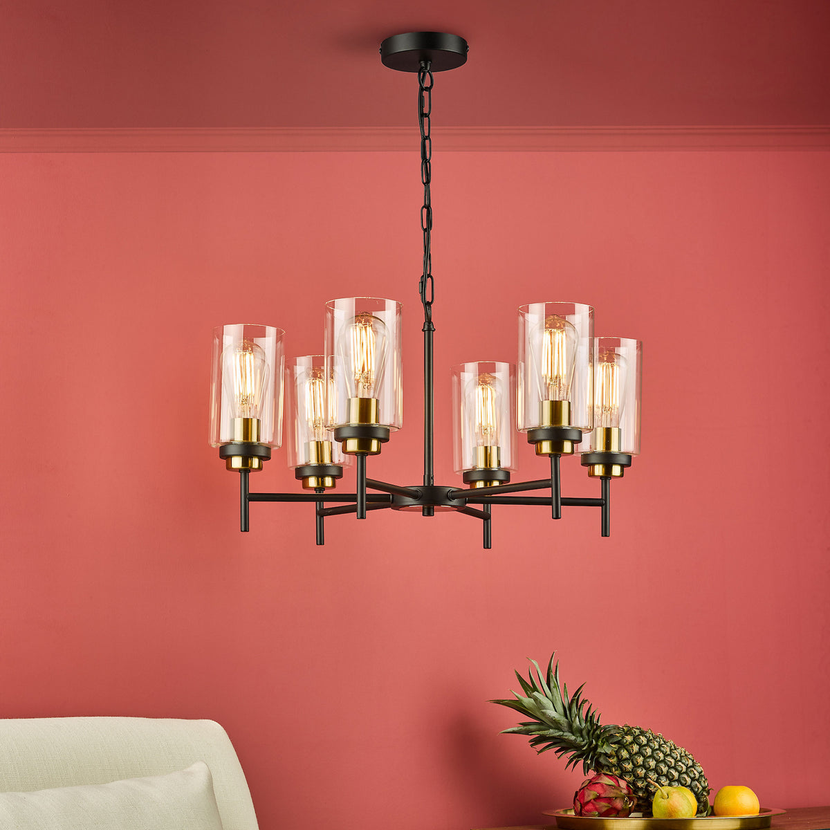 Black and gold chandelier with six clear glass shades and exposed bulbs, against a coral wall.