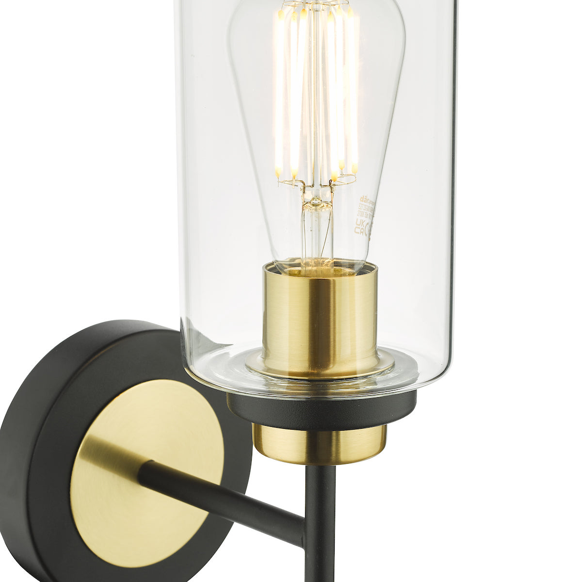 Close-up of a wall light with a black base, brass accents, and a clear glass shade housing an Edison bulb.