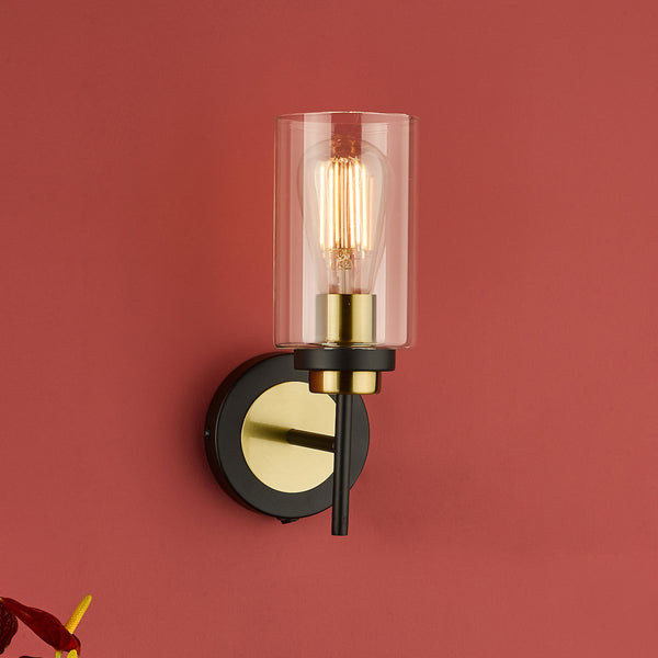 Modern wall sconce with a clear glass shade, exposed filament bulb, and a black and brass base.