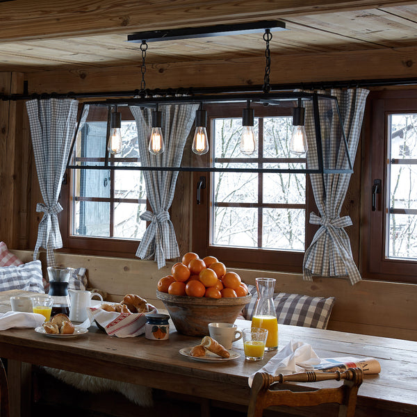 A rustic dining room with a wooden table set for breakfast, featuring croissants, coffee, and a bowl of oranges.