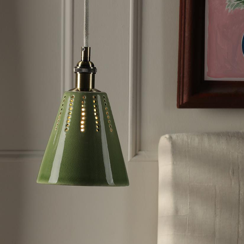 Green ceramic pendant light with perforated vertical lines hanging from a fabric cord