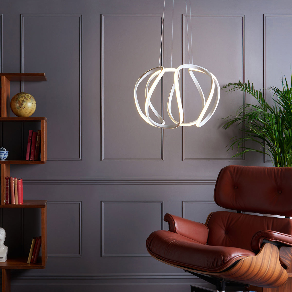 Modern living room with a brown leather chair, wooden bookshelf, and a unique, illuminated pendant light.