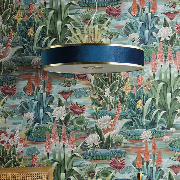 Blue velvet drum lampshade with gold trim against a botanical wallpaper with water lilies and red hot pokers.
