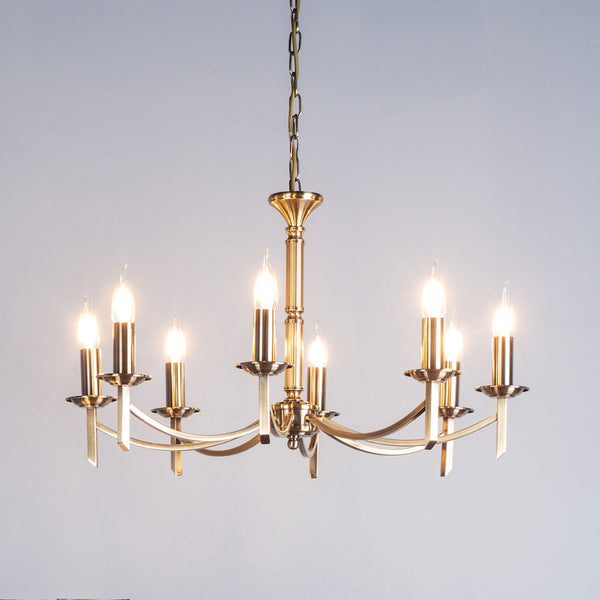 A brass chandelier with eight lit candle-style bulbs, hanging from a chain against a light background.