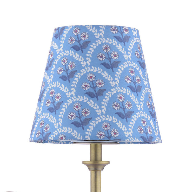 Blue tapered lamp shade with white and purple floral vine pattern on a brass base