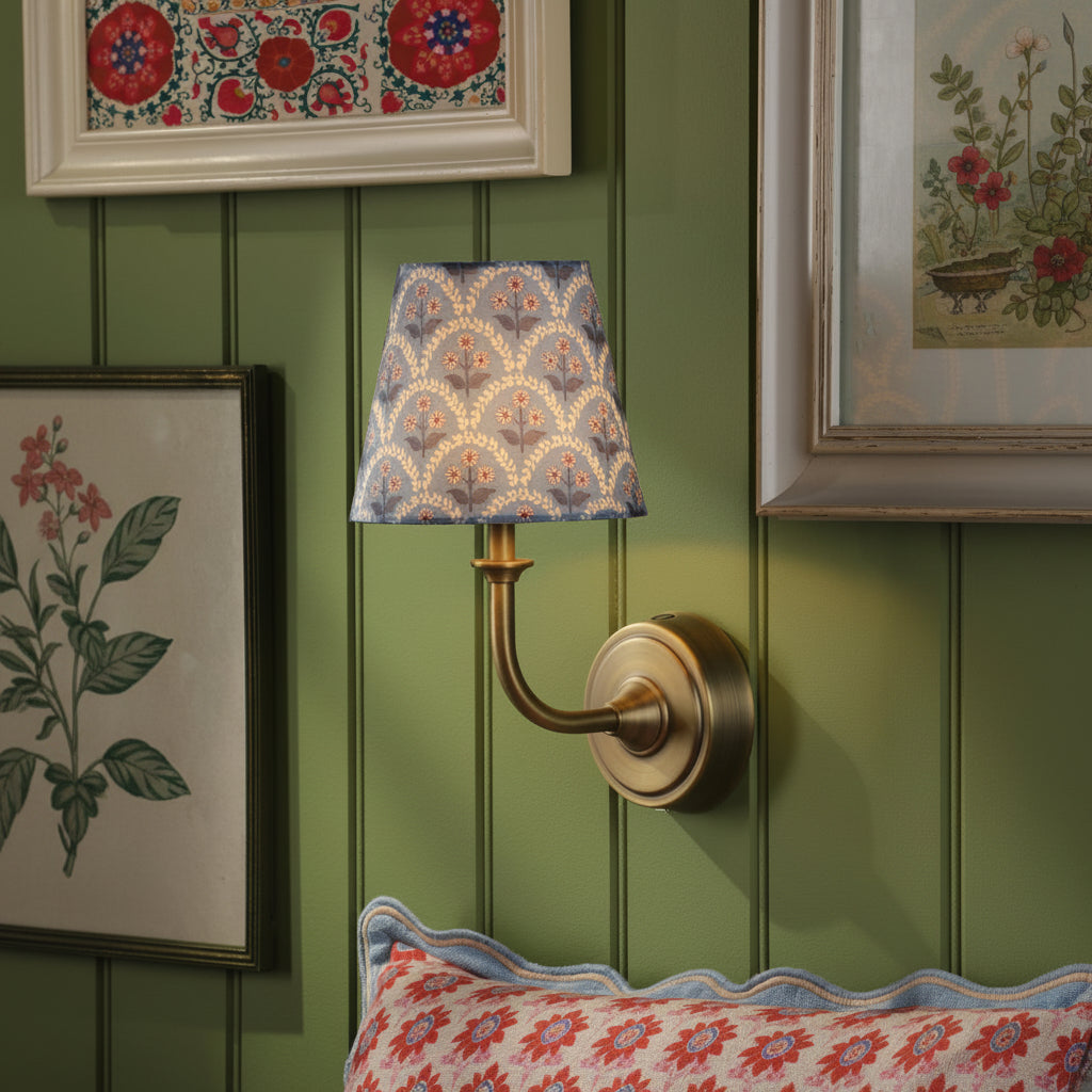 Brass wall sconce with a blue floral patterned fabric shade mounted on a green paneled wall