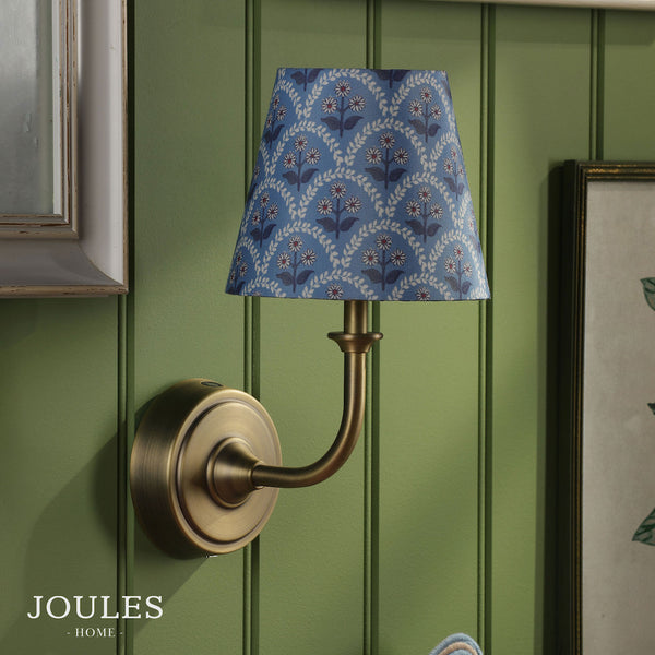 Joules Home wall lamp with a blue floral patterned shade and antique brass finish mounted on a green paneled wall