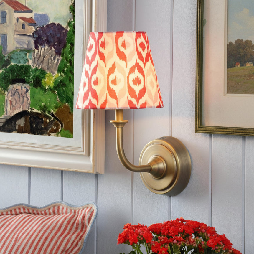 Brass wall sconce with a red and white patterned fabric shade mounted on a light blue paneled wall