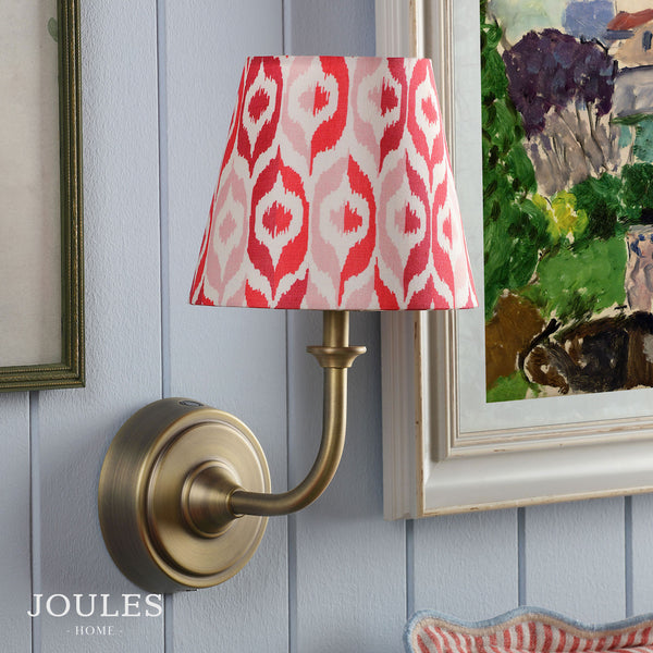 Joules Home wall lamp with a red and pink ikat patterned shade and antique brass finish arm