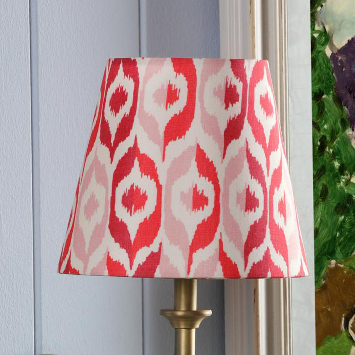 Tapered lamp shade with red and pink ikat pattern on a brass base