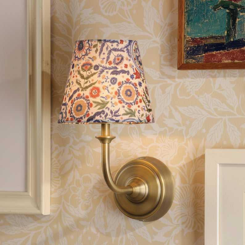 Joules Apsley rechargeable wall light in matt antique brass with a floral print cotton shade mounted on patterned wall