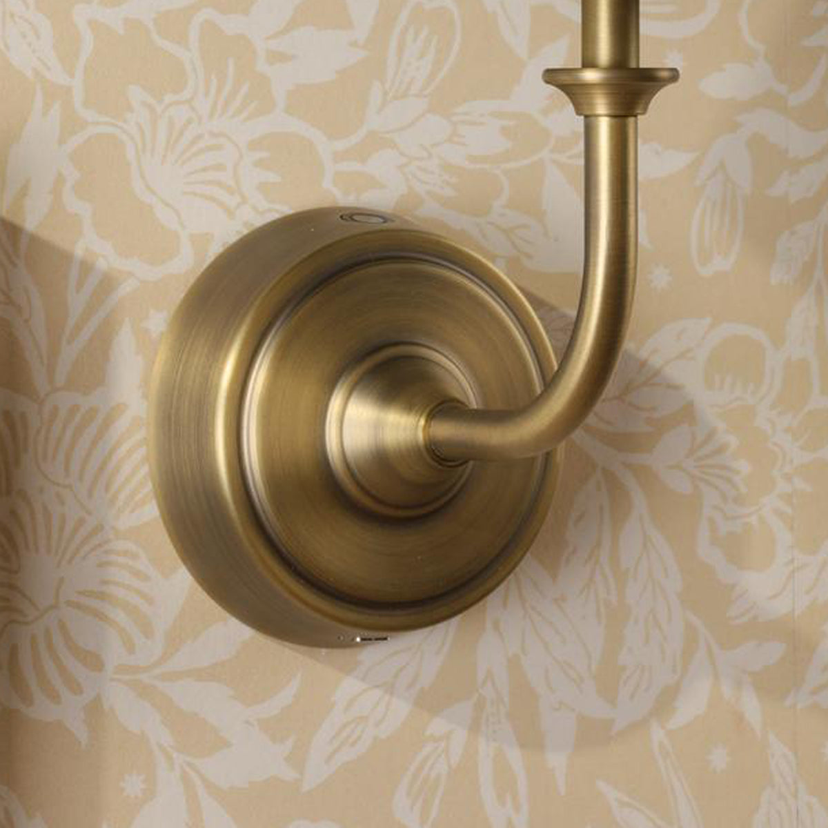 Antique brass wall sconce base mounted on floral patterned wallpaper