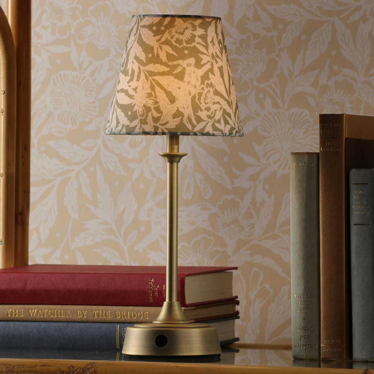 Brass table lamp with a patterned fabric shade sitting on a stack of books