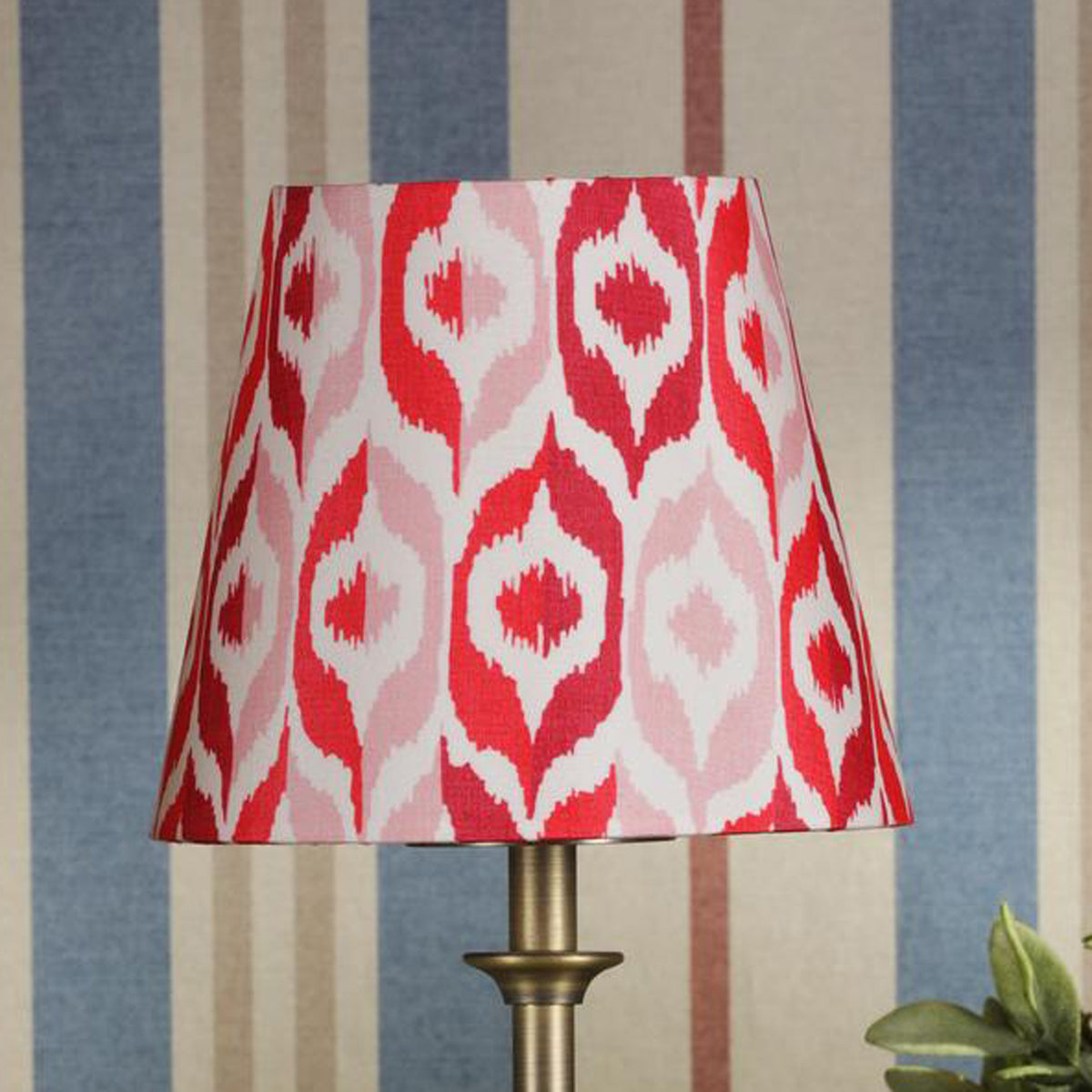 Tapered lampshade with a red and pink ikat pattern on a brass lamp base