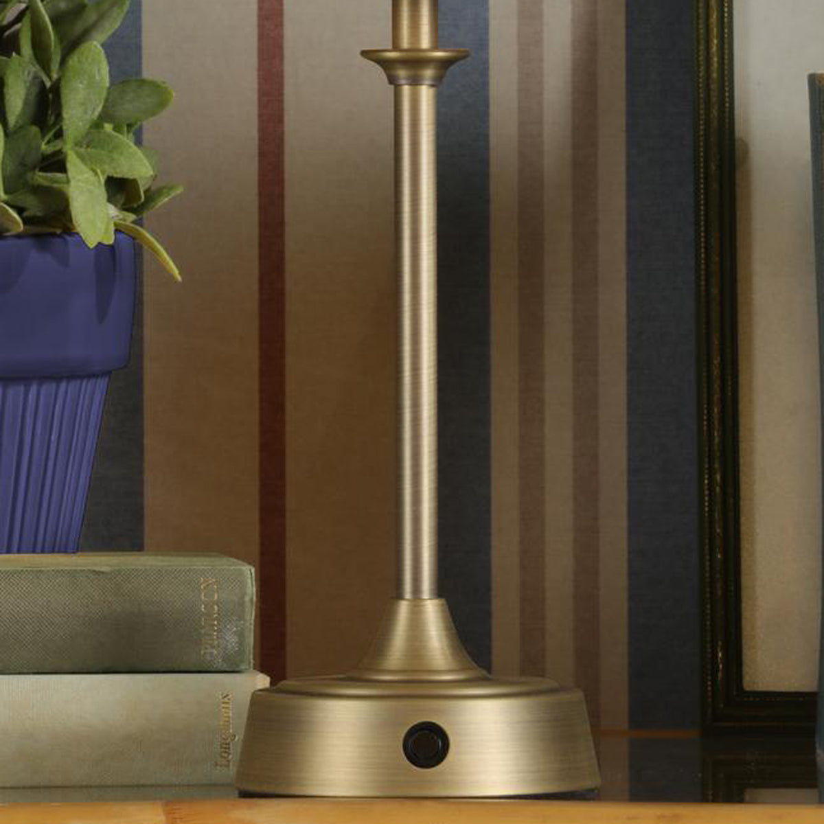 Antique brass lamp base with push button switch on a table with books and a blue plant pot