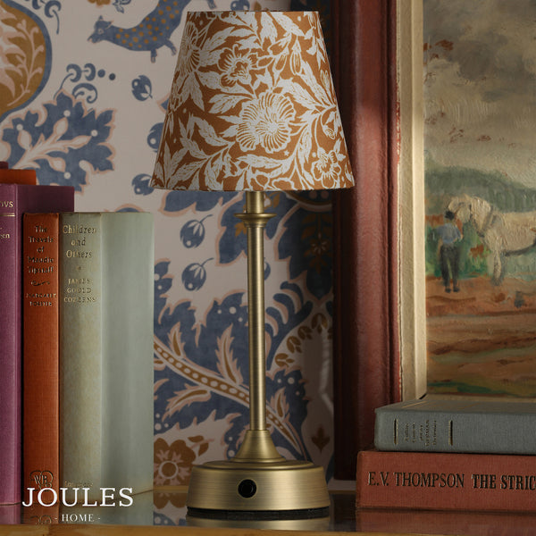 Joules Home brass table lamp with a floral patterned shade sitting on a shelf next to books